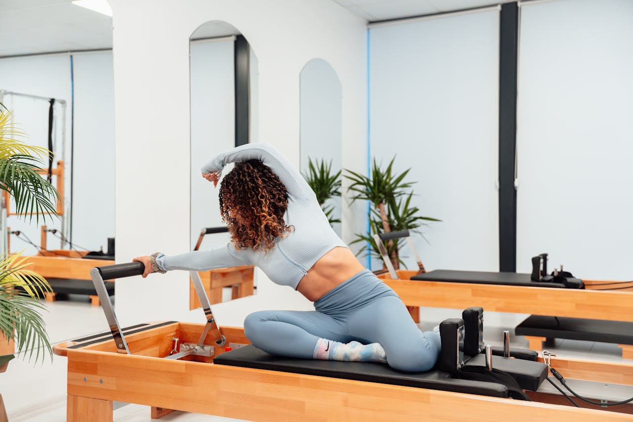 Woman practicing Pilates on a reformer machine in a modern studio, demonstrating stretching and fitness.